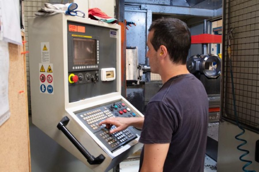 Técnico operando control CNC para el mecanizado de precisión en cuerpos de válvulas industriales como parte de un mantenimiento predictivo.