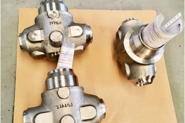 Tres componentes mecanizados con etiquetas de lote y hoja de control, listos para verificación dimensional con IMEs/CMM en Sala de Metrología.