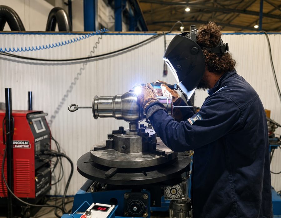 Soldador trabajando en un torno industrial durante un proceso de soldadura especializada en Asimer Group.